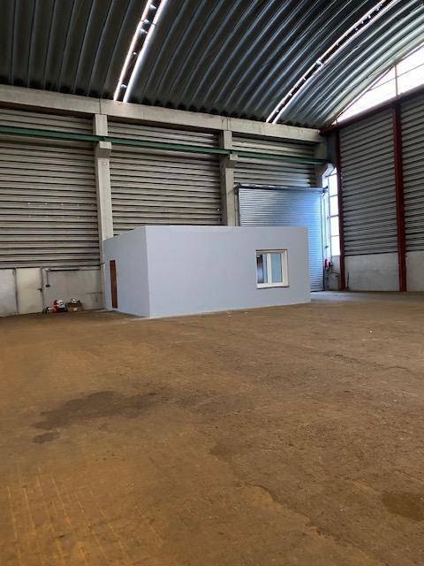 Weitläufige Lagerhalle mit einer kleinen, eingebauten Büro- oder Technikbox und Rolltoren im Hintergrund.