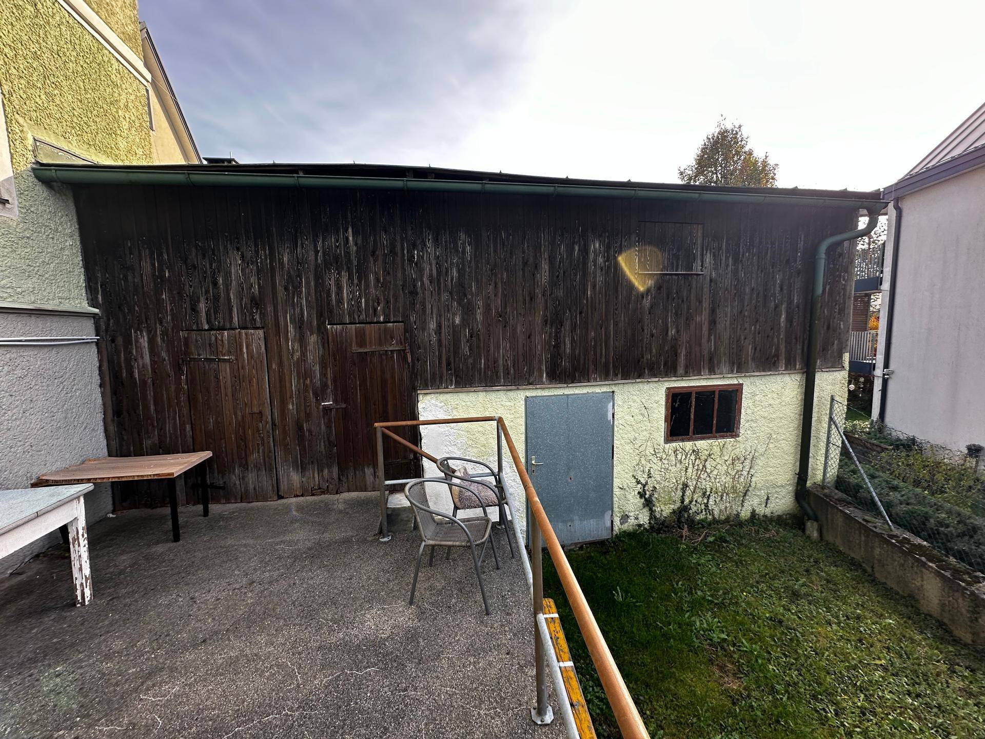 Rustikales Nebengebäude mit Holzwänden und kleiner Betonfläche mit Gartenmöbeln im Freien.