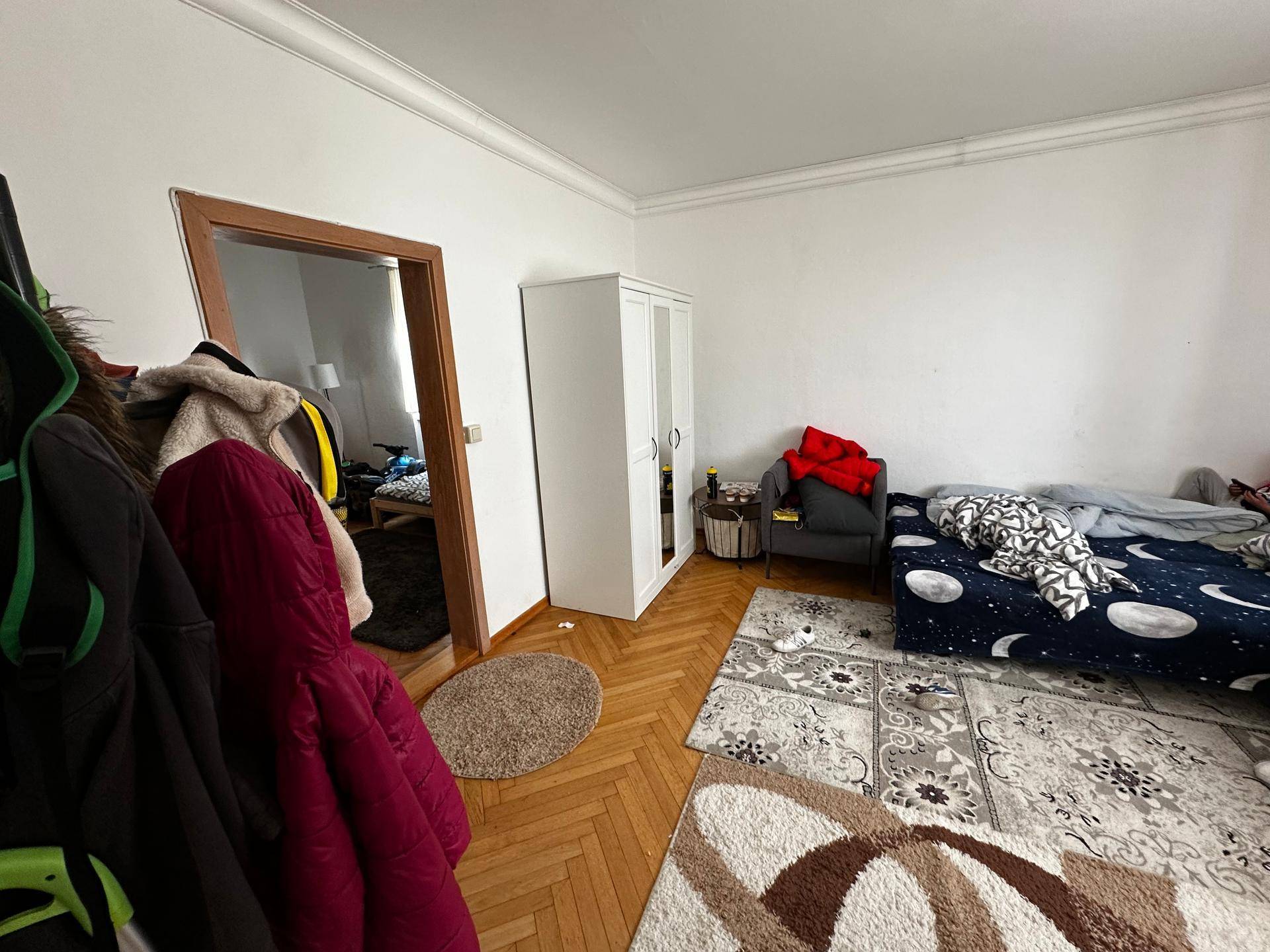 Schlafzimmer mit Parkettboden, einem Bett mit gemusterter Decke und einem weißen Kleiderschrank.