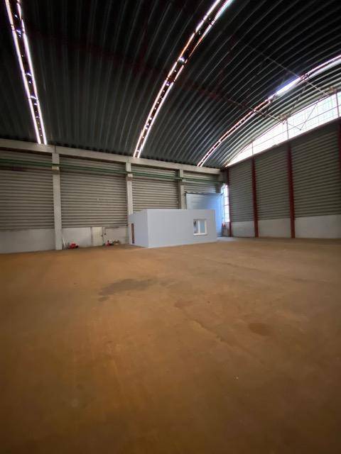 Geräumige Industriehalle mit einer freistehenden, hellgrauen Box und großen Rolltoren an den Seitenwänden.