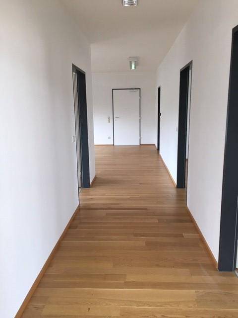 Langer, heller Flur mit Holzboden und weißen Wänden, der zu mehreren Räumen führt.