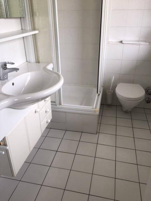Helles Badezimmer mit Dusche, Waschbecken und WC, komplett gefliest in Weiß.