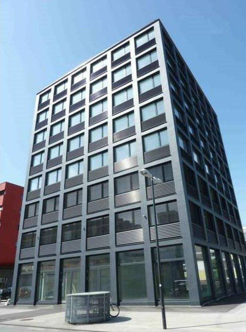 Ansicht eines modernen Bürogebäudes mit vielen Fenstern und dunkler Fassade unter blauem Himmel.