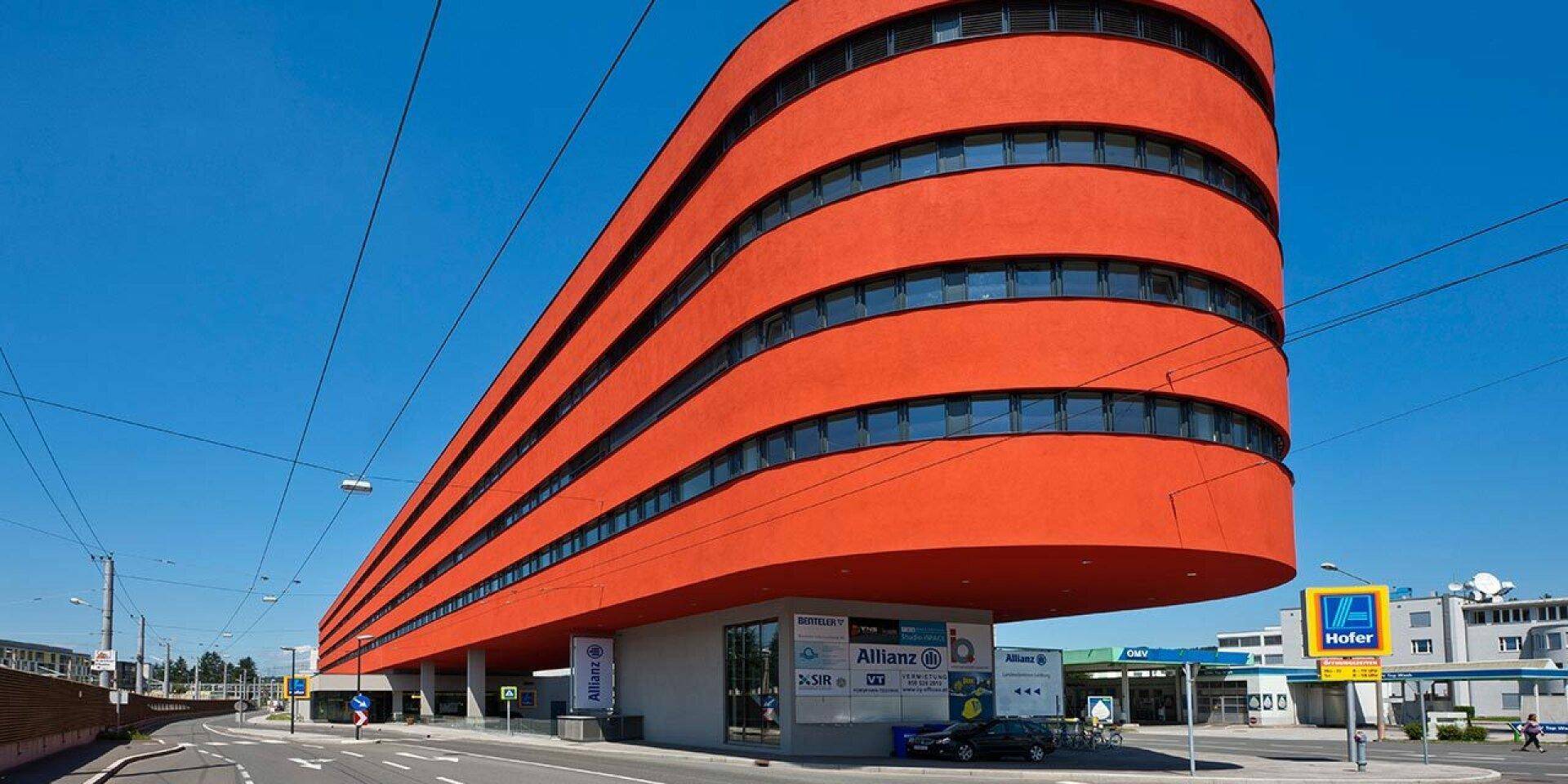 Markantes modernes Gebäude mit abgerundeter oranger Fassade und durchgehenden Fensterbändern an einer Straße.
