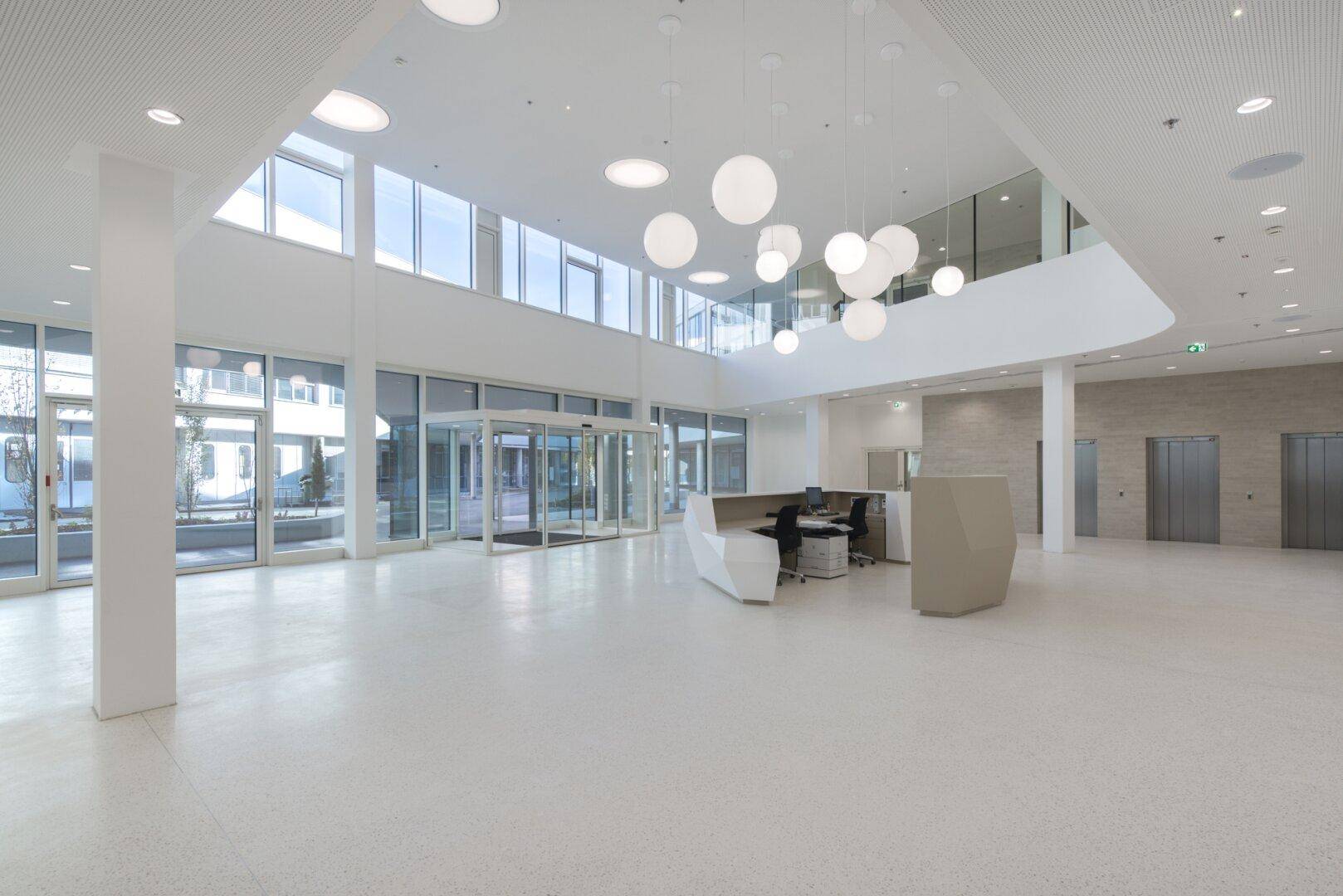 Geräumige und helle Lobby mit hoher Decke, großen Fenstern, modernem Empfangstresen und Aufzügen.