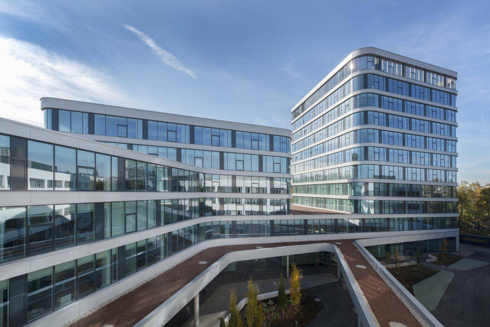 Architektonisch anspruchsvolle Bürogebäude mit reflektierenden Glasfassaden und verbundenen Übergängen im Außenbereich.