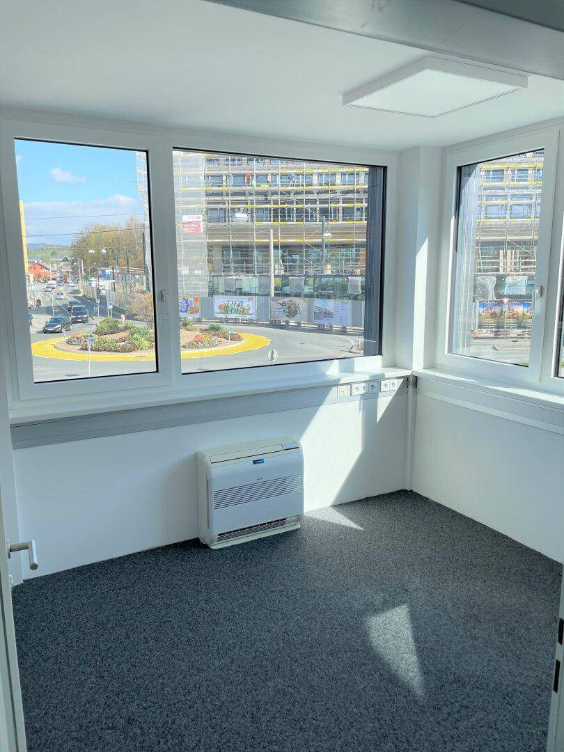 Kleiner Eckraum mit großen Fenstern, grauem Teppichboden und Blick auf die Straße und Baustelle.
