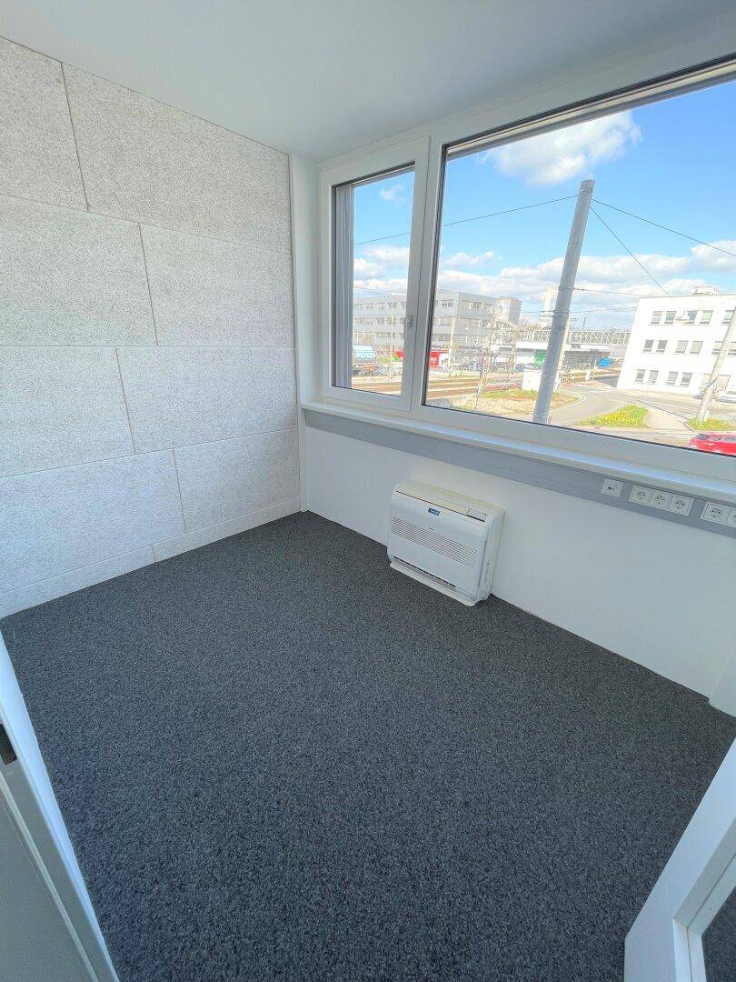 Kleiner Büroraum mit grauem Teppich, strukturierter Wandverkleidung und weitem Stadtblick.