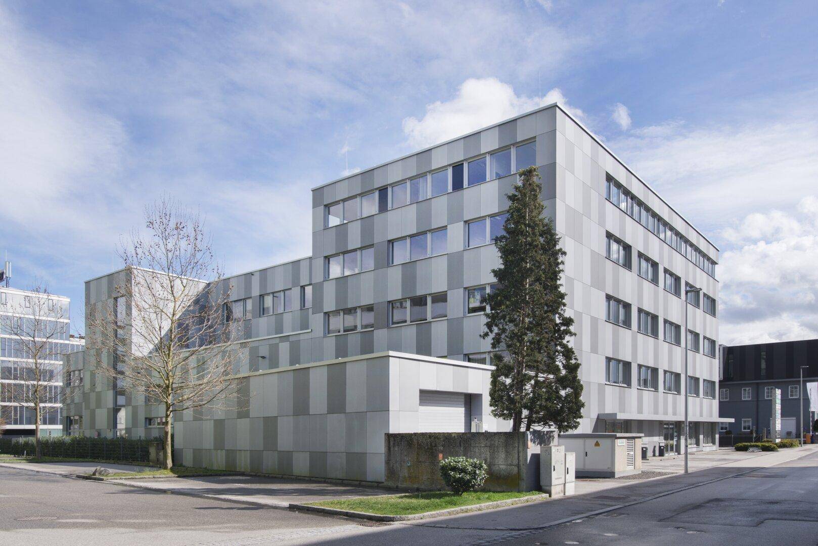 Ansicht des modernen Bürogebäudes von der Seite mit Bäumen und Parkplätzen im Vordergrund.