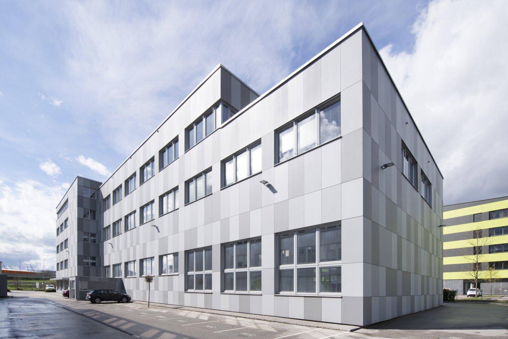 Seitliche Ansicht des Bürogebäudes mit gestreifter Fassade und weiteren Gebäuden im Hintergrund.