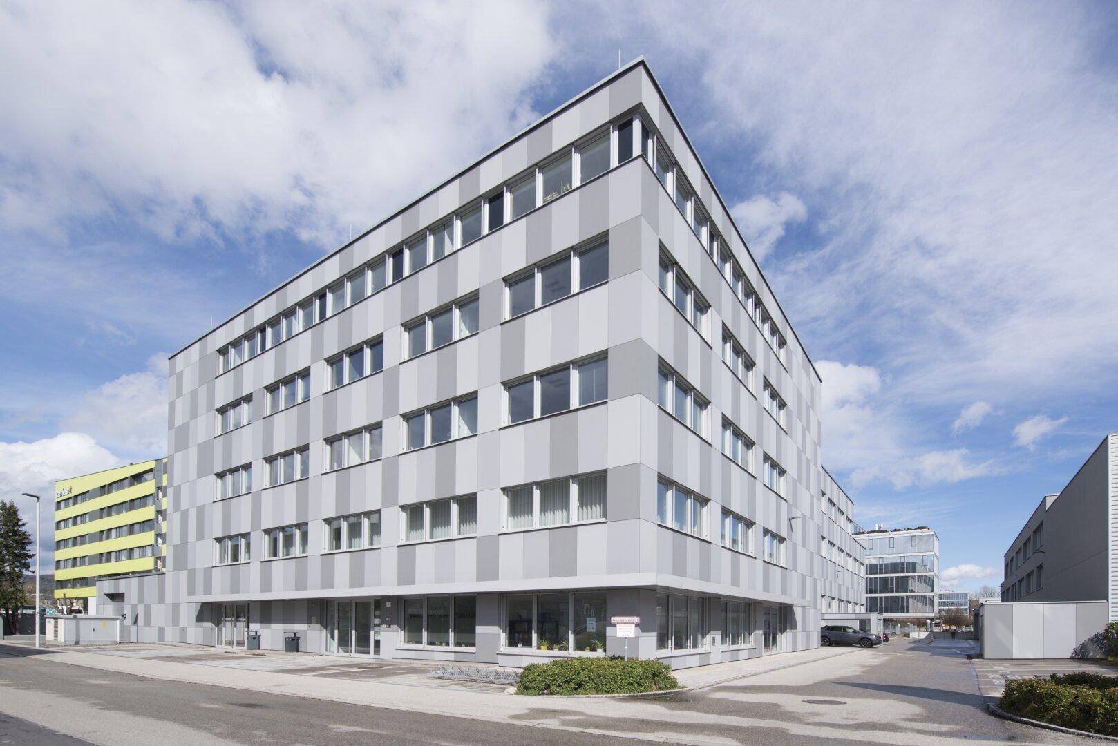 Weitwinkelansicht eines modernen Bürokomplexes mit gestreifter Fassade und umliegenden Parkplätzen.