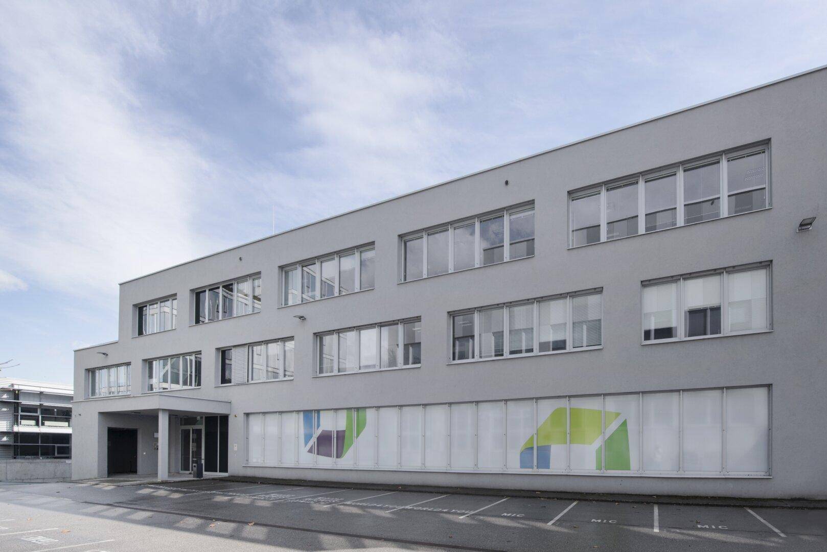 Ansicht des modernen Geschäftsgebäudes von der Seite mit Parkplätzen und klarem Himmel.