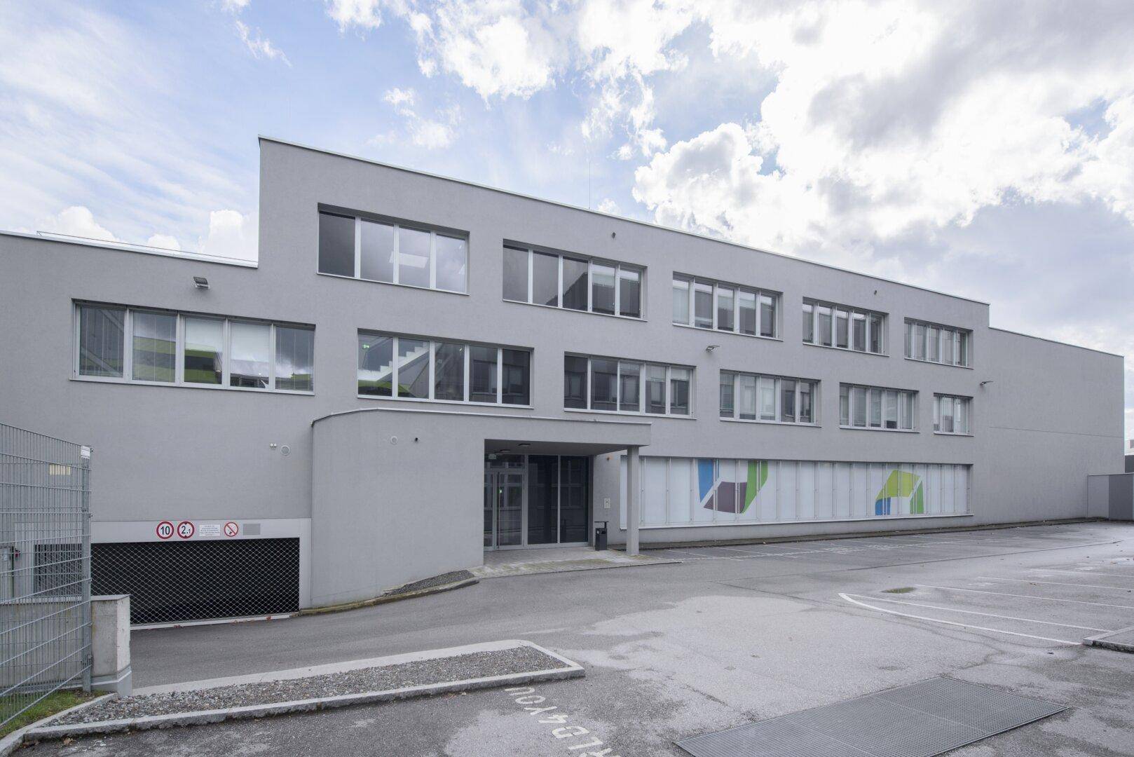 Modernes Geschäftsgebäude mit Eingangsbereich und Zufahrt zur Tiefgarage, unter blauem Himmel.
