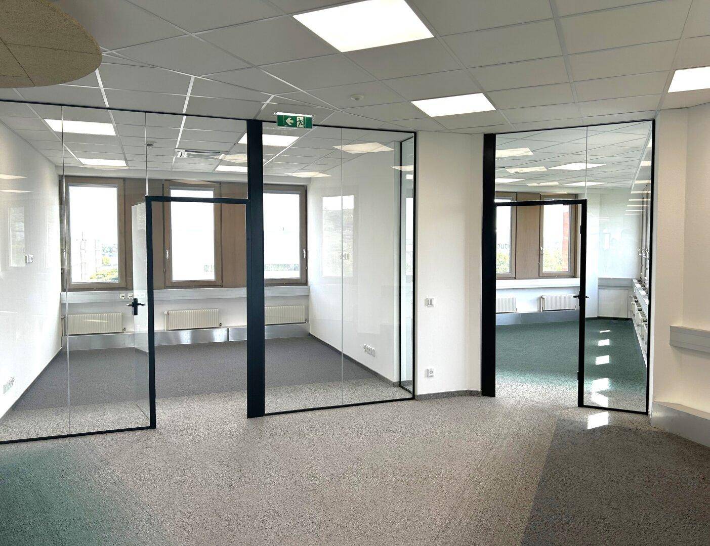 Heller Büroraum mit raumhohen Glaswänden und großen Fenstern, bietet eine moderne Arbeitsumgebung.