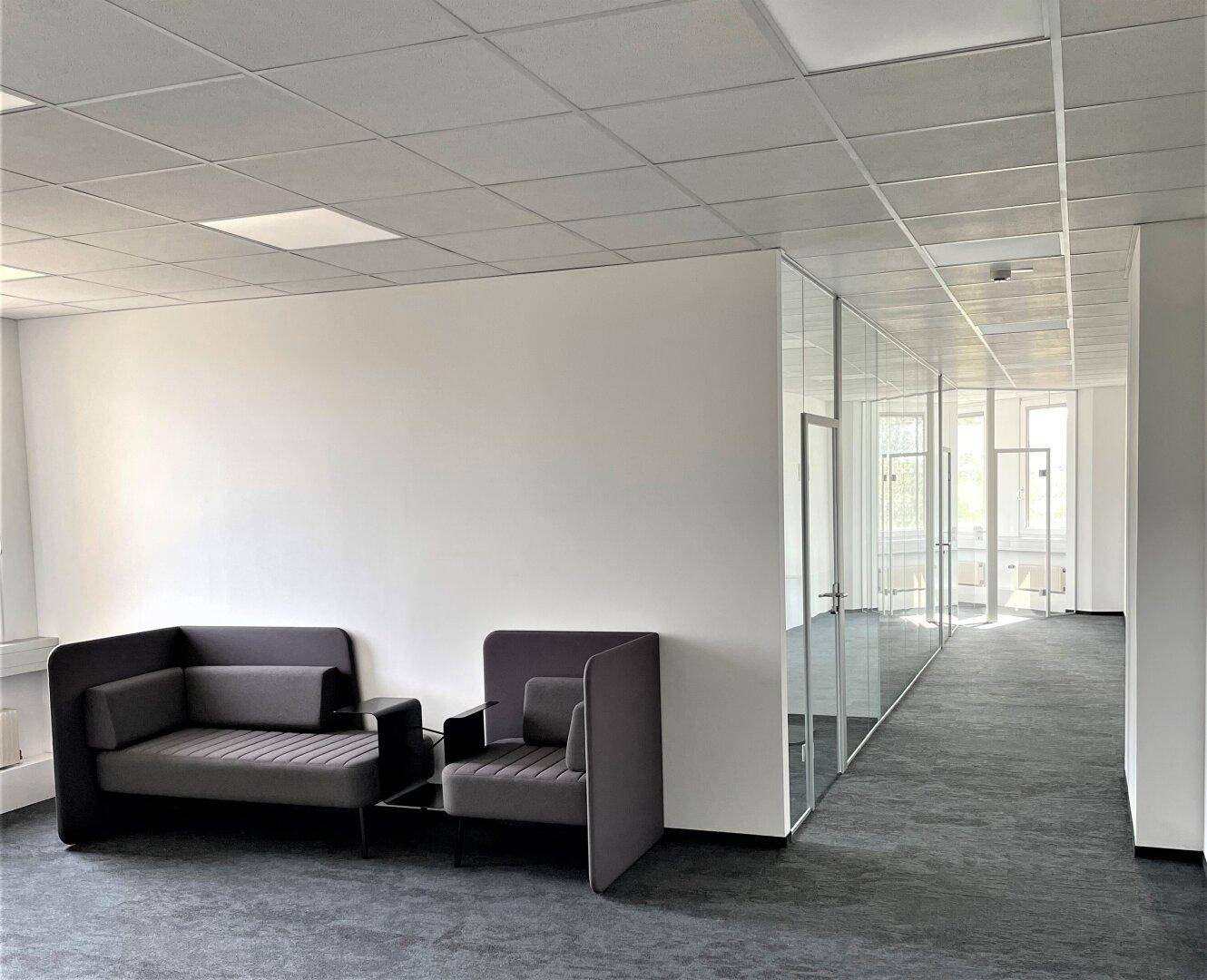 Gemütlicher Loungebereich in einem modernen Büro mit bequemen Sofas und Glaswänden zum Flur.
