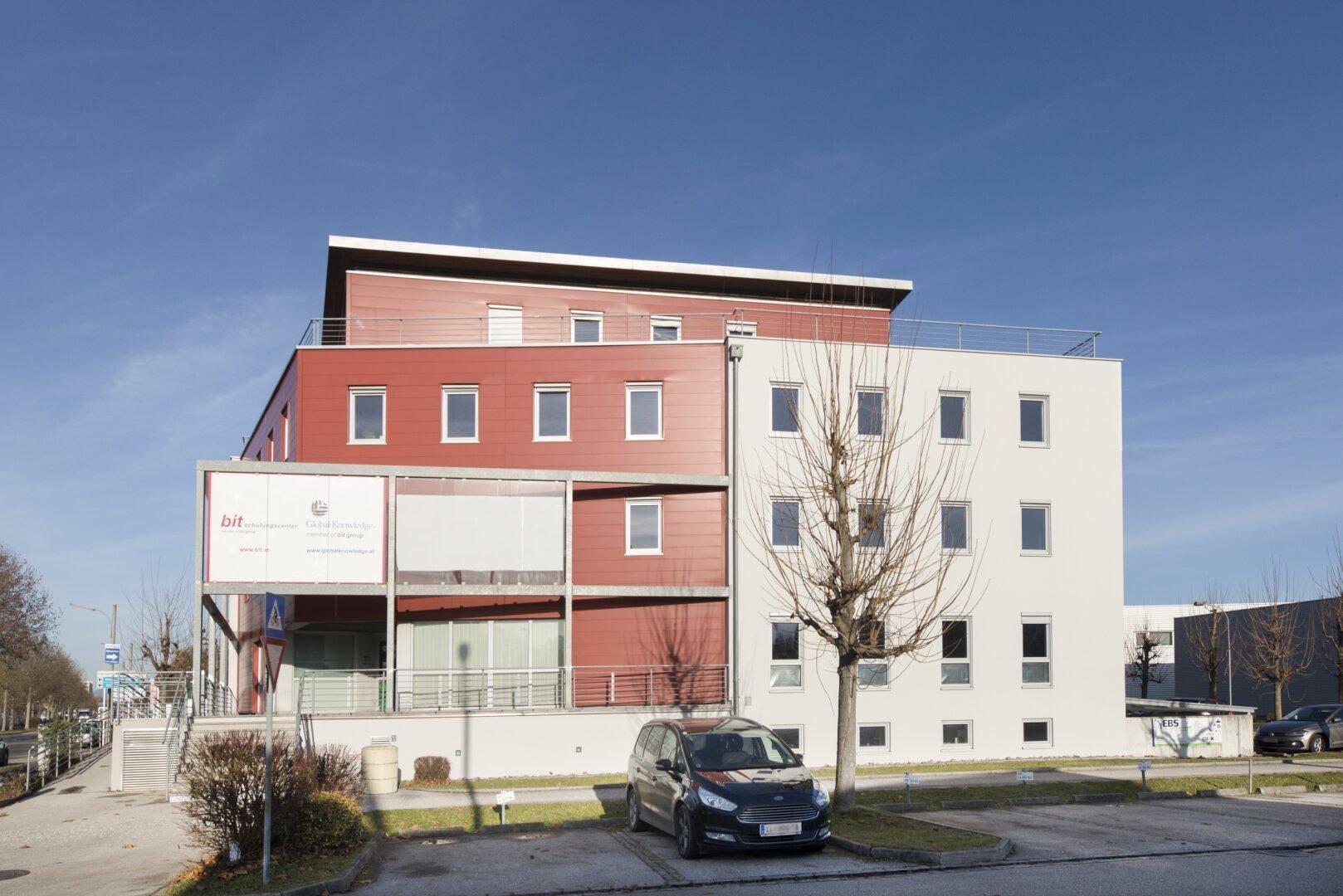 Ansicht des modernen Geschäftsgebäudes mit Parkplatz und klarer Architektur unter strahlendem Himmel.