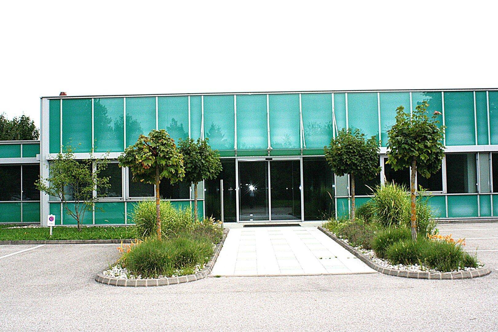 Modernes Gebäude mit markanter grüner Fassade und gepflegtem Eingangsbereich mit Bepflanzung und Parkmöglichkeiten.