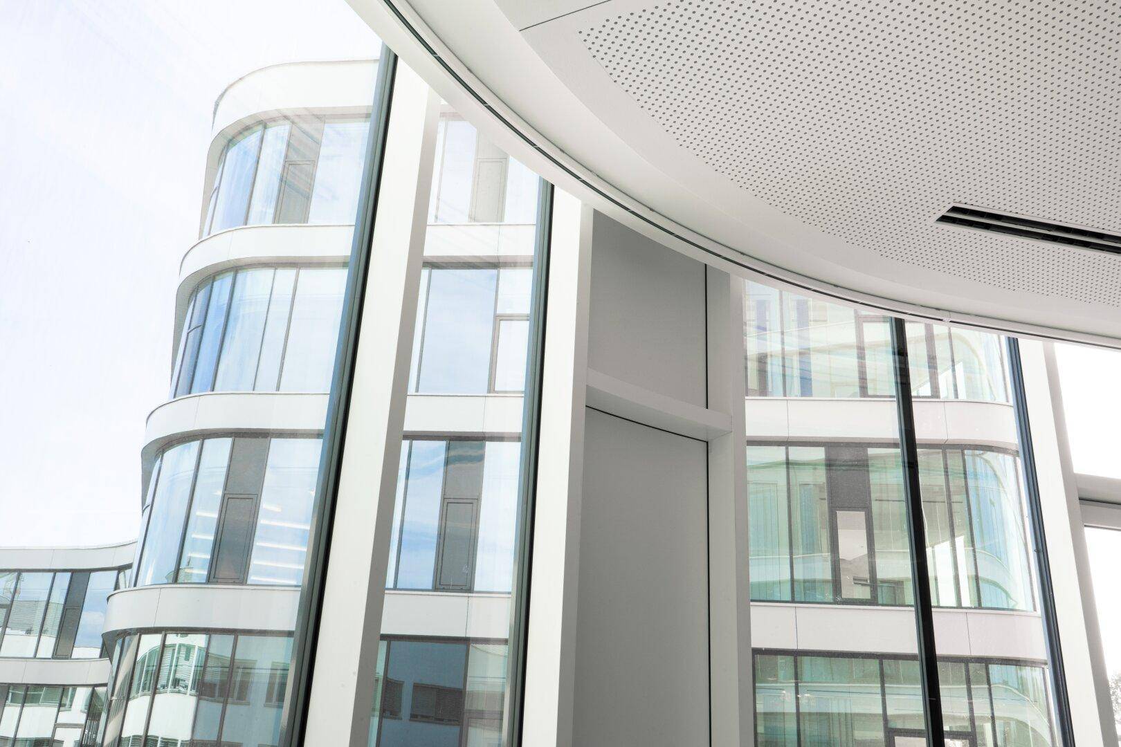 Moderne Gebäudeansicht mit geschwungenen Glasfassaden und reflektierenden Fenstern, zeigt zeitgenössische Architektur.