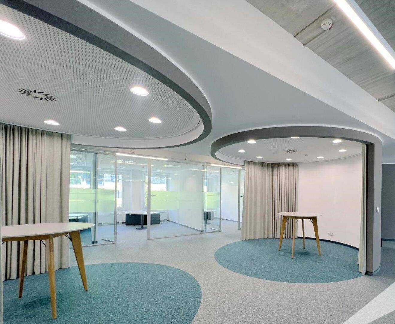 Modernes Interieur mit geschwungenen Decken, Teppichböden und Glaswänden, ideal für Empfänge oder Veranstaltungen.