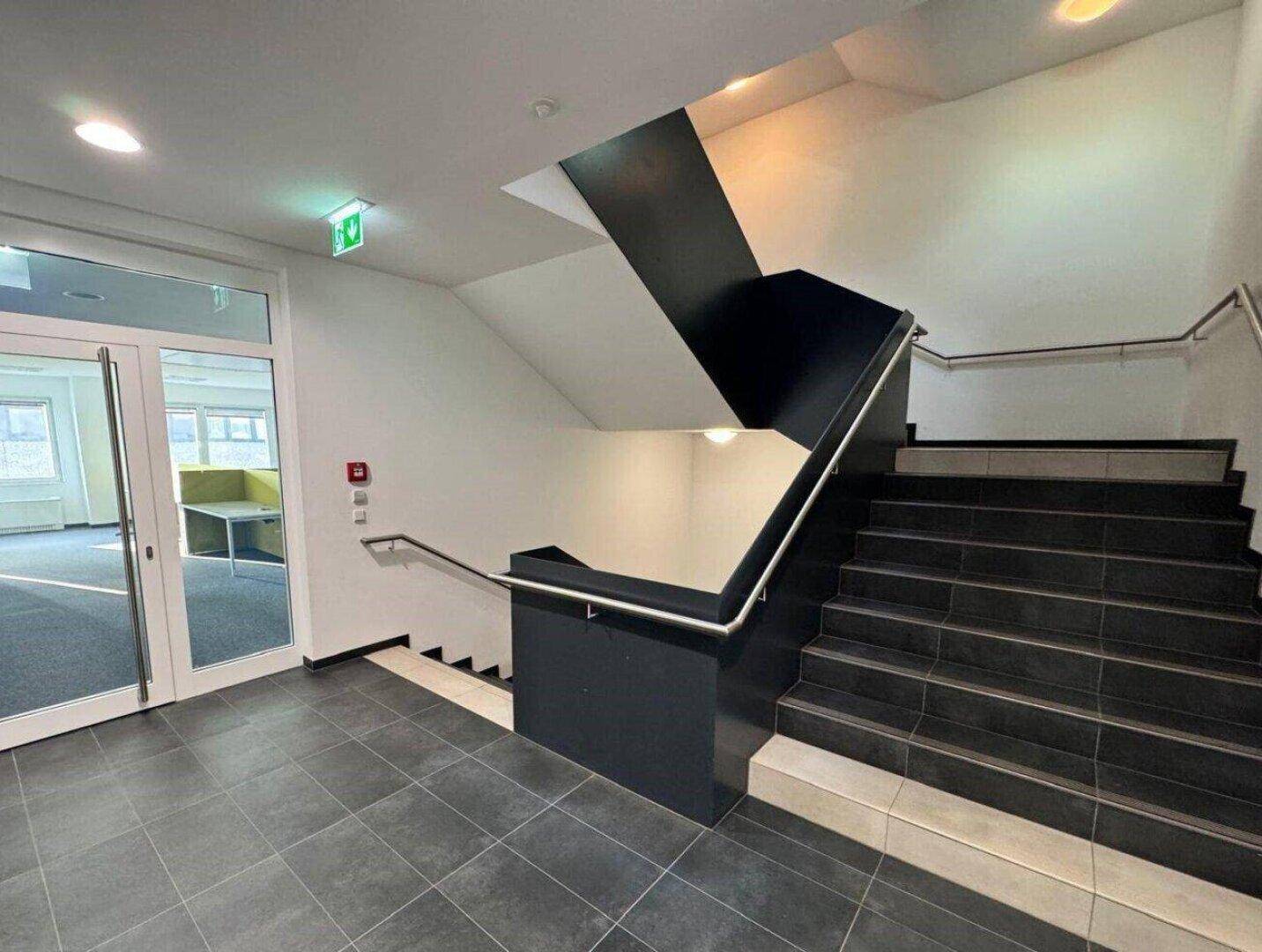 Modernes Treppenhaus mit dunklen Fliesenstufen und Metallgeländer, das zu weiteren Büroflächen führt.