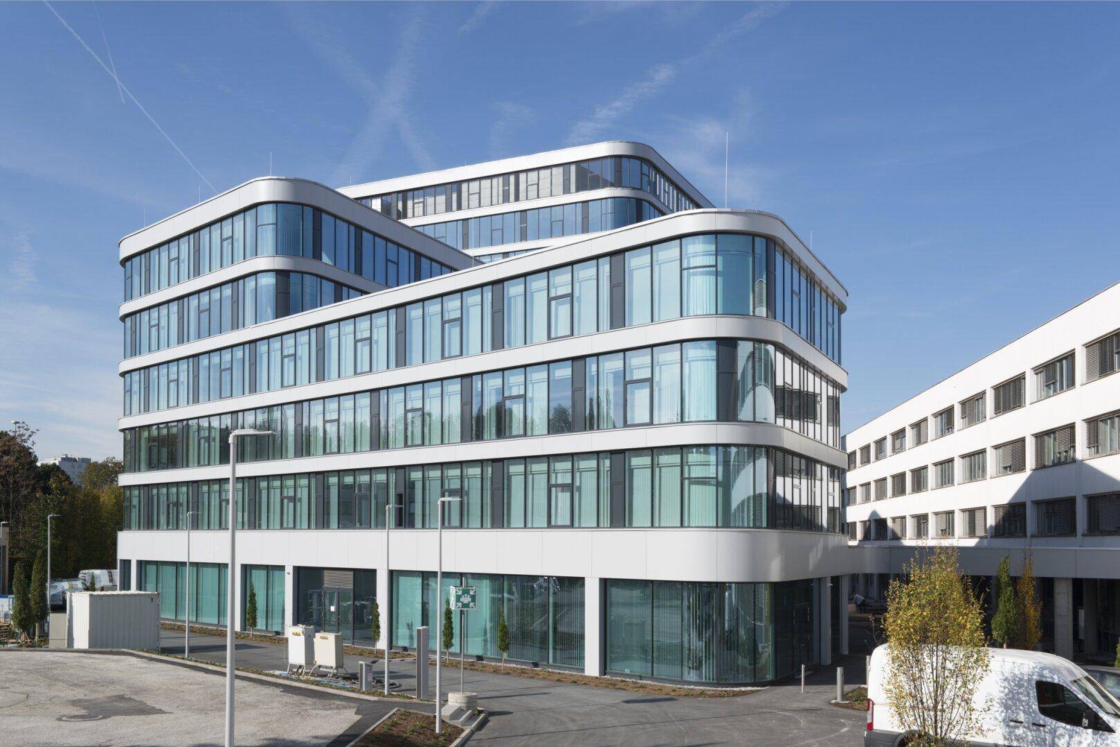 Ansicht eines modernen Bürokomplexes mit geschwungenen Fassaden und großen Fensterflächen an einem sonnigen Tag.