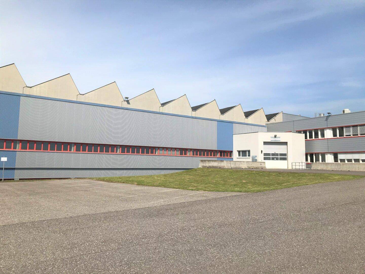 Außenansicht eines Industriegebäudes mit blauer und grauer Fassade sowie einem gezackten Dach.
