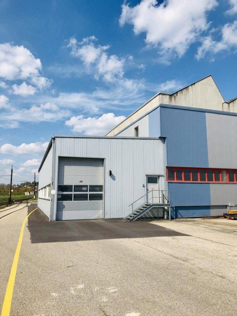 Seitenansicht eines Industriegebäudes mit Rolltor, blauer Fassade und Zugang zu Bahngleisen.