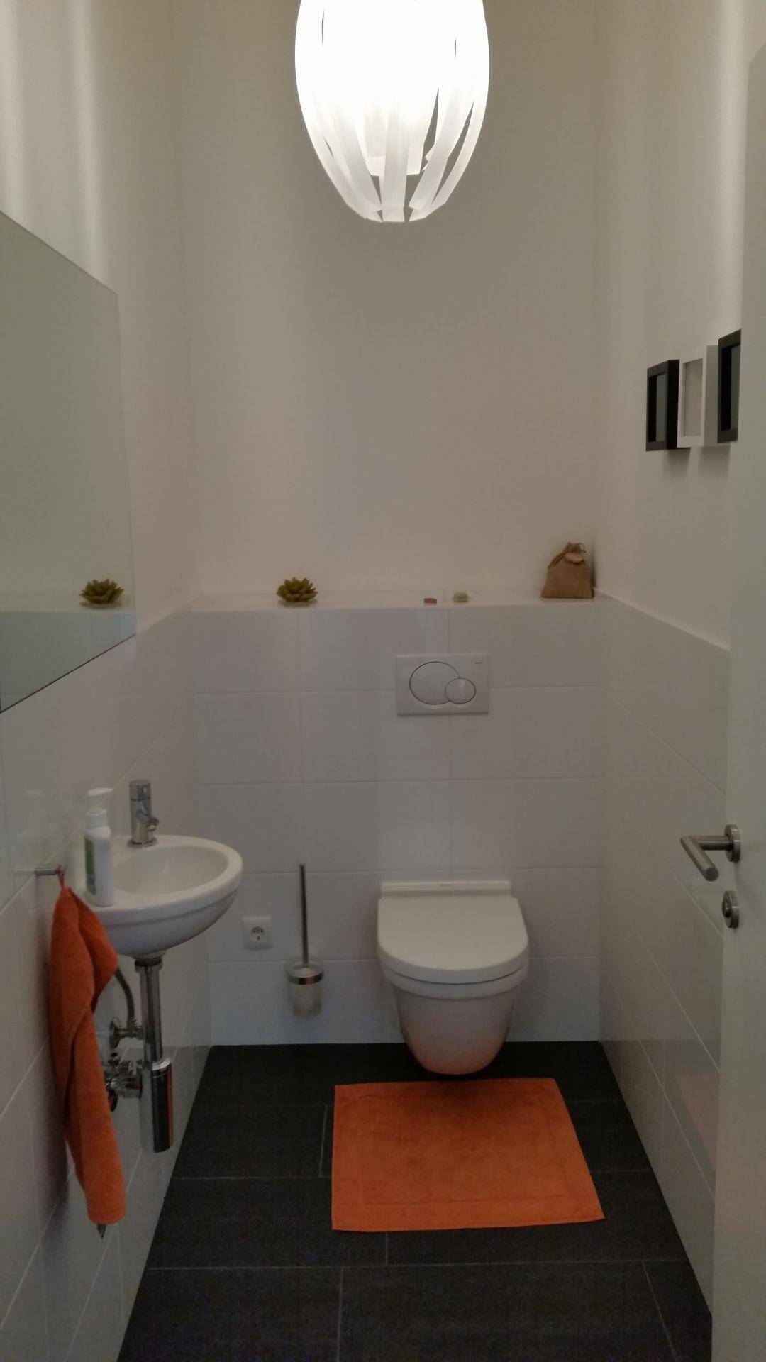 Kleines Gäste-WC mit wandhängender Toilette, Waschbecken und dunklen Bodenfliesen.