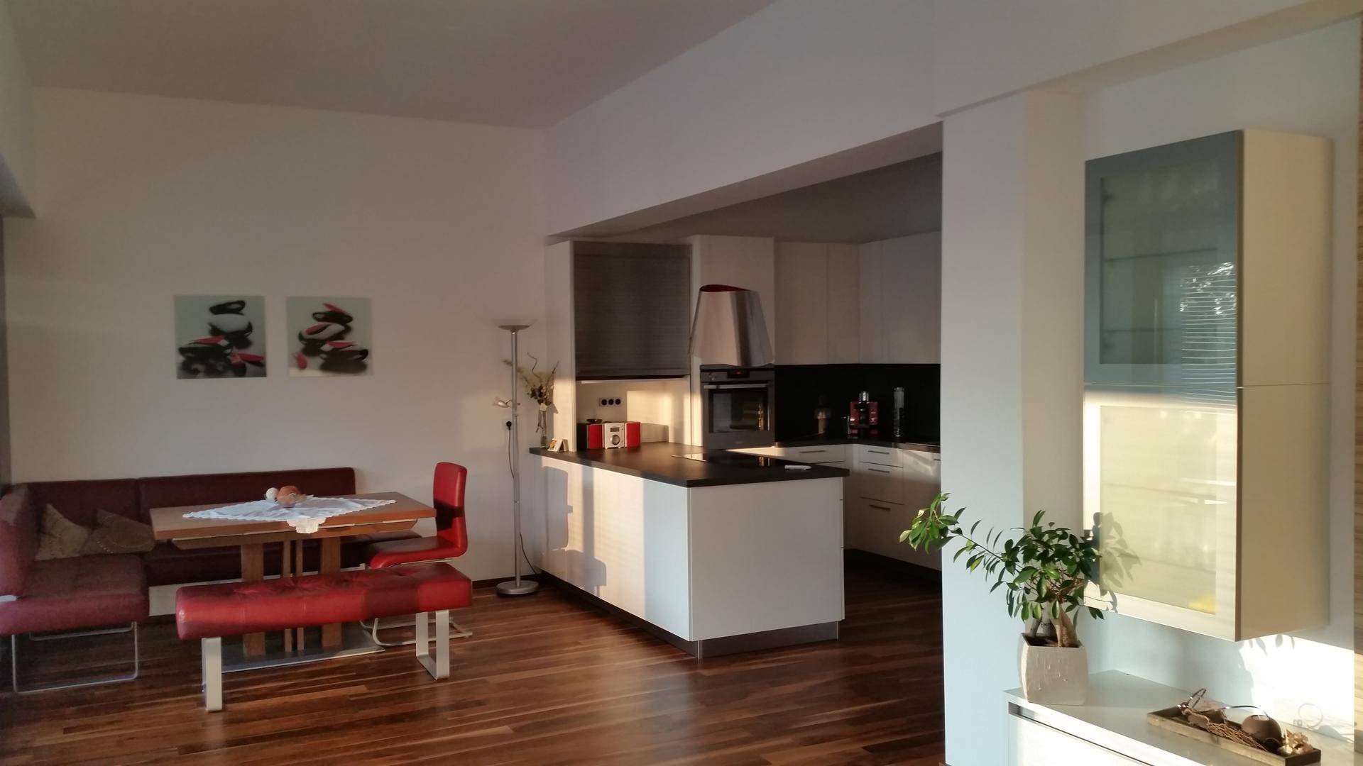 Offener Wohn- und Essbereich mit Holzboden und moderner Einbauküche in Weiß.