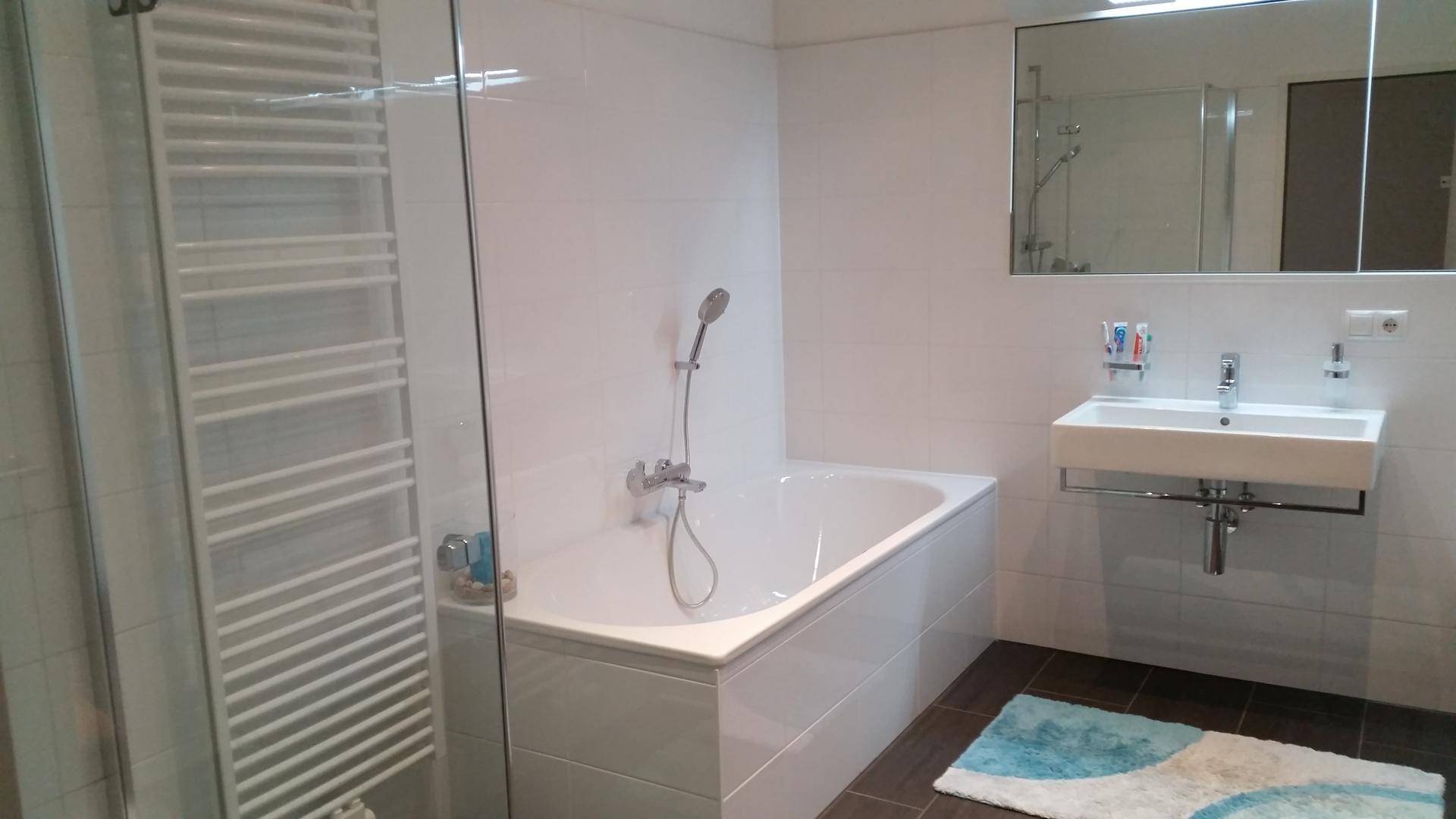 Modernes Badezimmer mit Badewanne, Duschbereich und beheiztem Handtuchhalter.