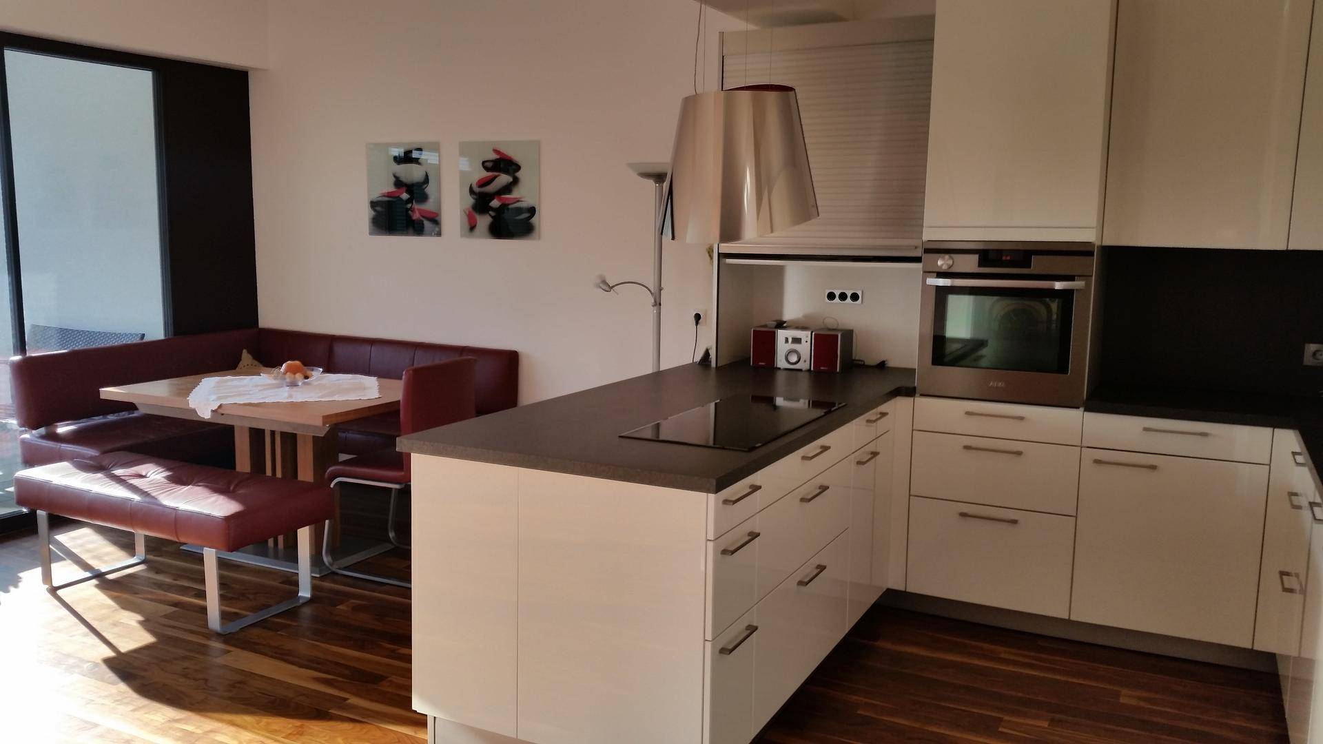 Moderne weiße Küche mit Kochinsel, integriertem Backofen und Essbereich mit Eckbank.