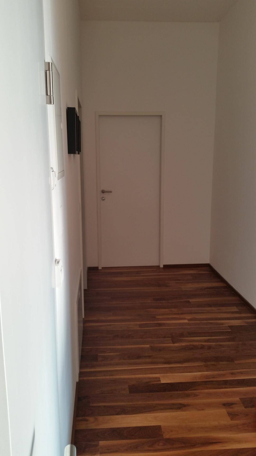 Heller Flur mit Holzboden und weißer Tür, der zu den weiteren Räumen führt.