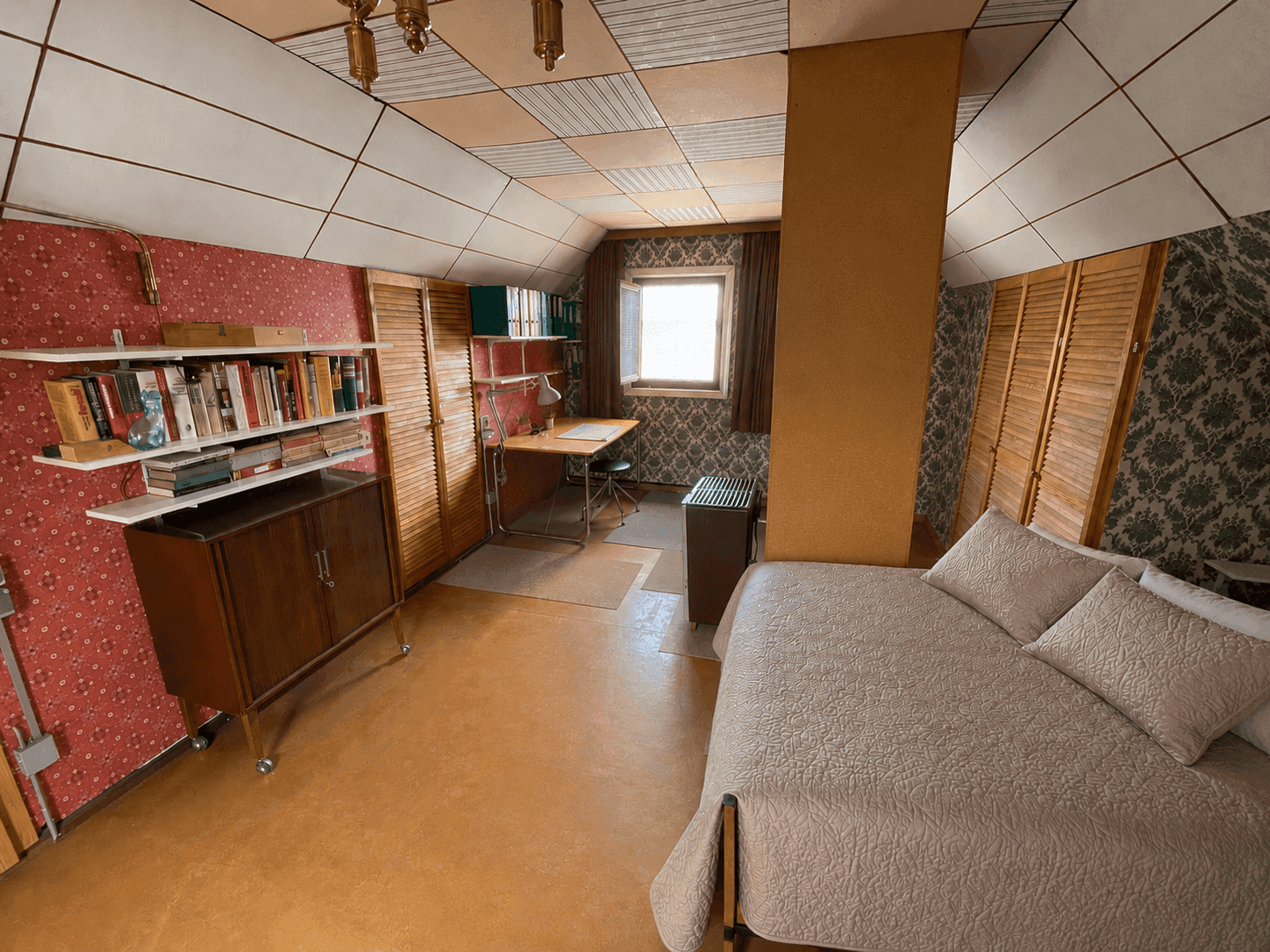 Dachgeschosszimmer mit Schlafbereich, Schreibtisch und Bücherregal, charakterisiert durch schräge Wände und Decken.