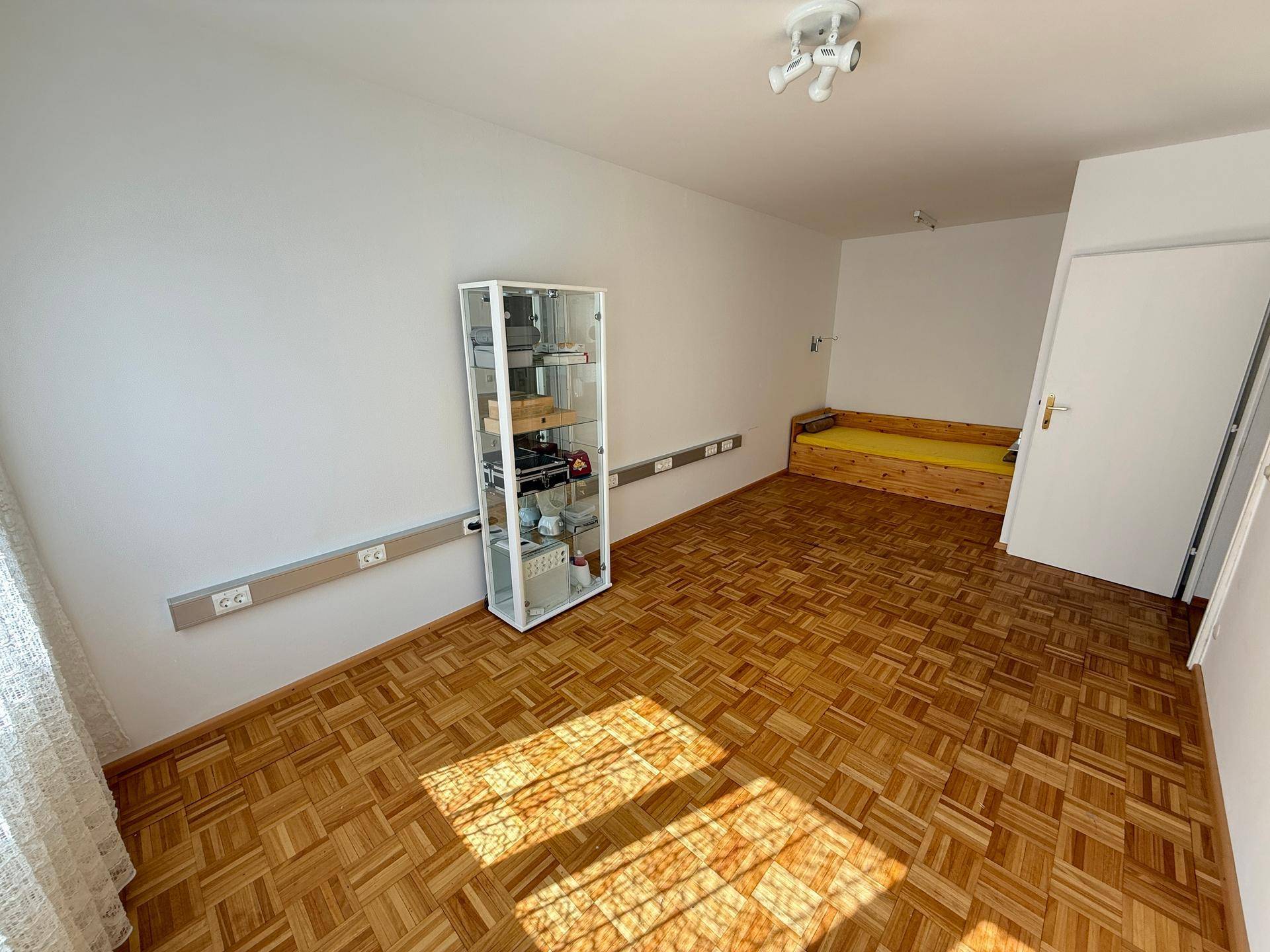 Helles Schlafzimmer mit Parkettboden, weiß gestrichenen Wänden und einer einfachen Bettnische.