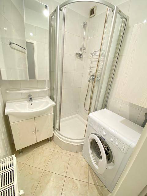 Modernes Badezimmer mit Duschkabine, Waschbecken und Waschmaschine, komplett gefliest.