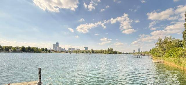 Weiter Blick über den See mit einer beeindruckenden Stadtsilhouette am Horizont unter einem bewölkten Himmel.