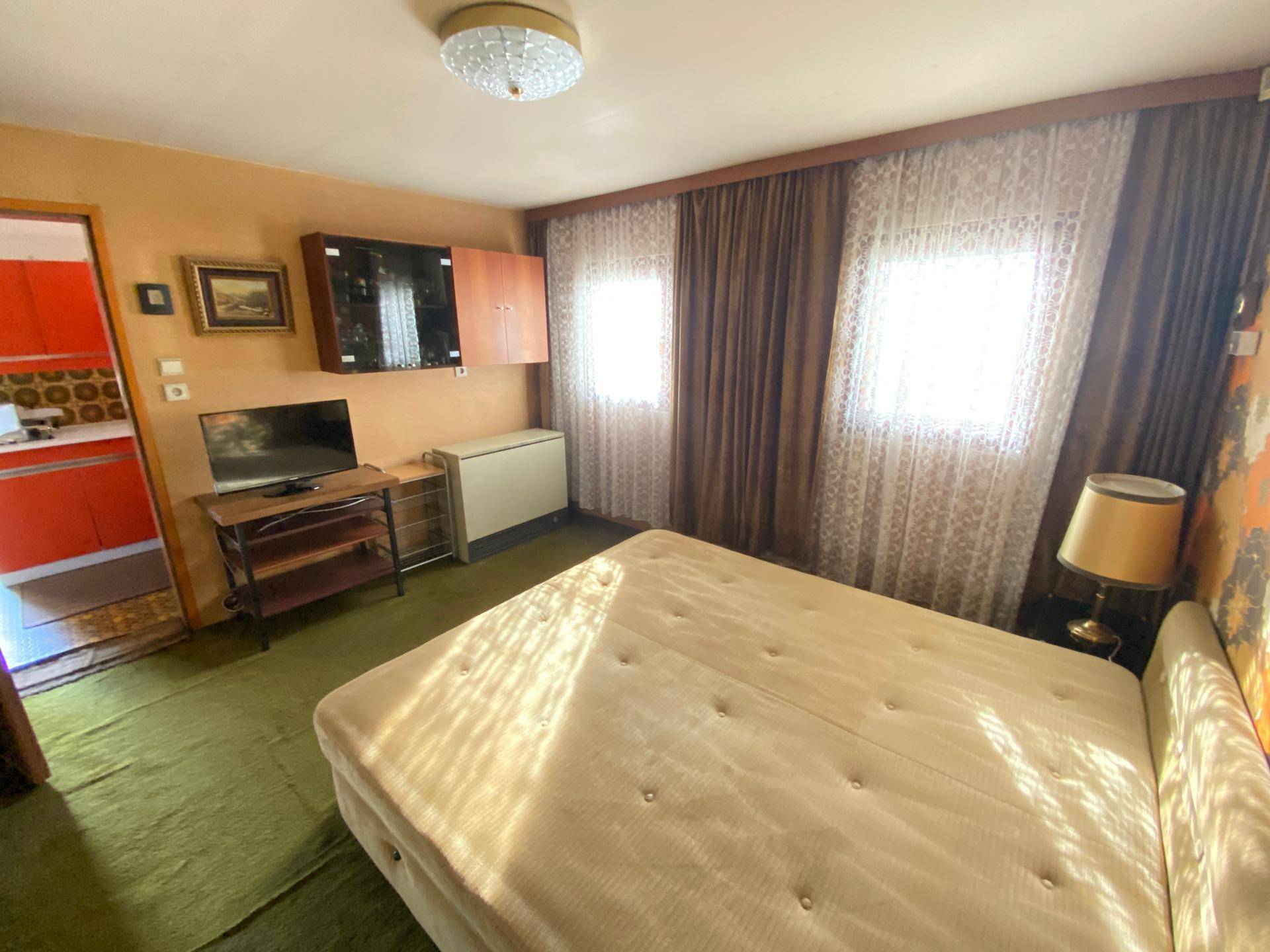 Schlafzimmer mit floraler Tapete, grünem Teppich und Blick in die angrenzende Küche, bietet viel Tageslicht.