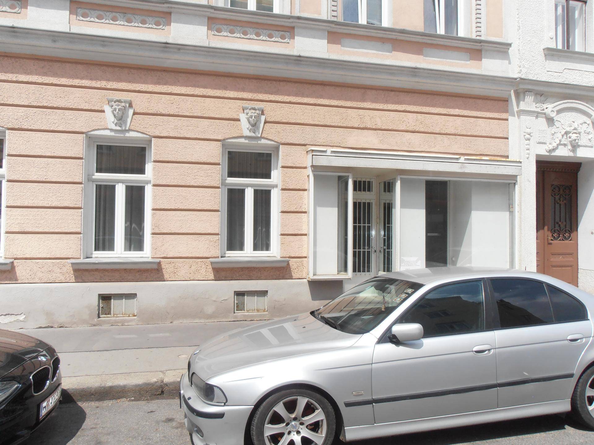 Detailansicht der Fassade eines Altbaus mit Fenstern und einem geparkten silbernen Auto im Vordergrund.