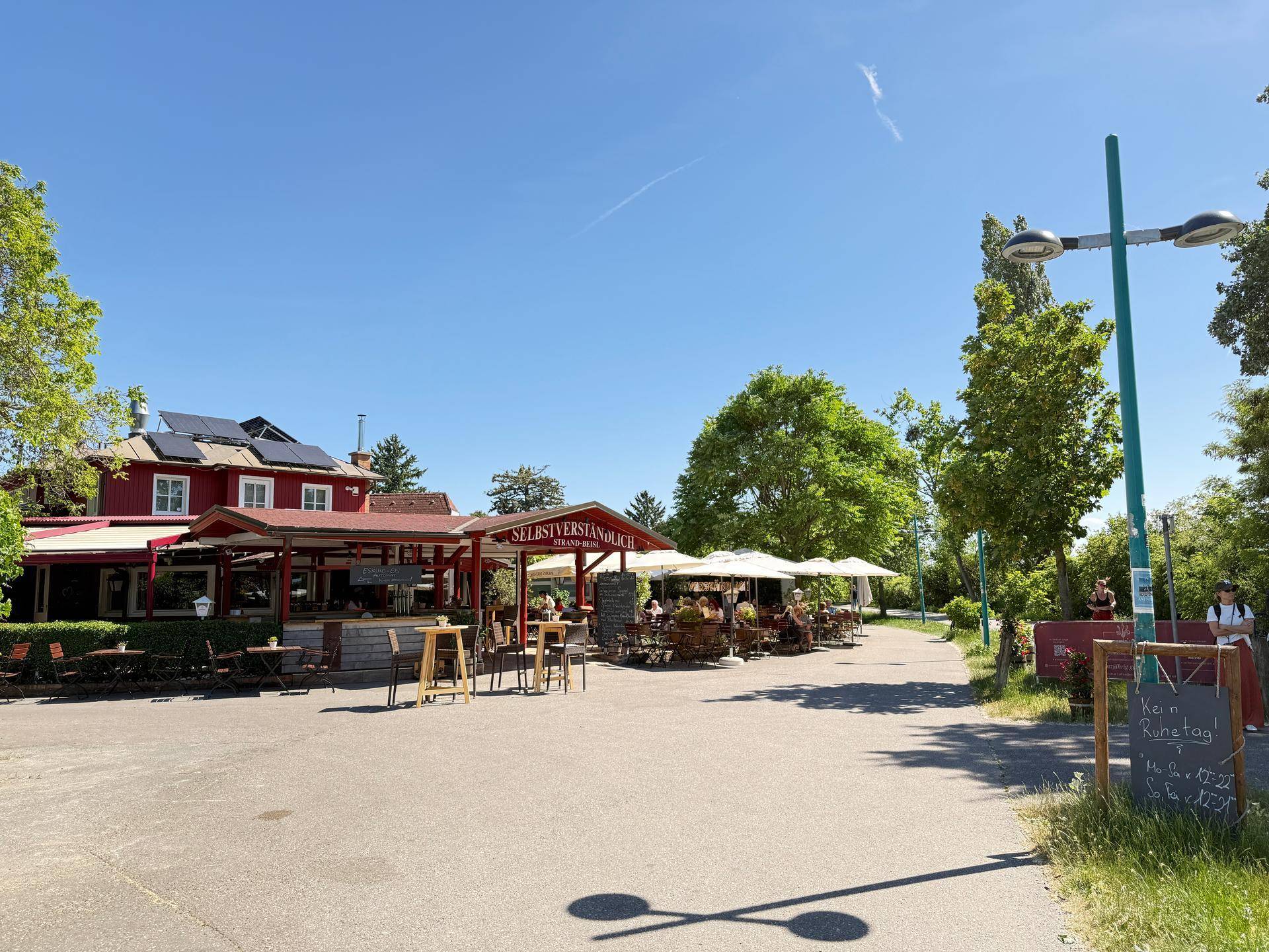 Weitläufiger Außenbereich eines Restaurants mit vielen Sitzgelegenheiten und Sonnenschirmen unter blauem Himmel.