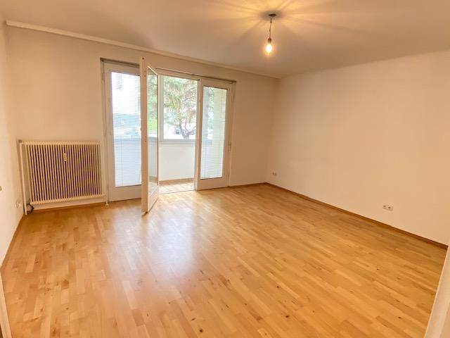 Geräumiges Wohnzimmer mit Parkettboden und Zugang zu einem verglasten Balkon.