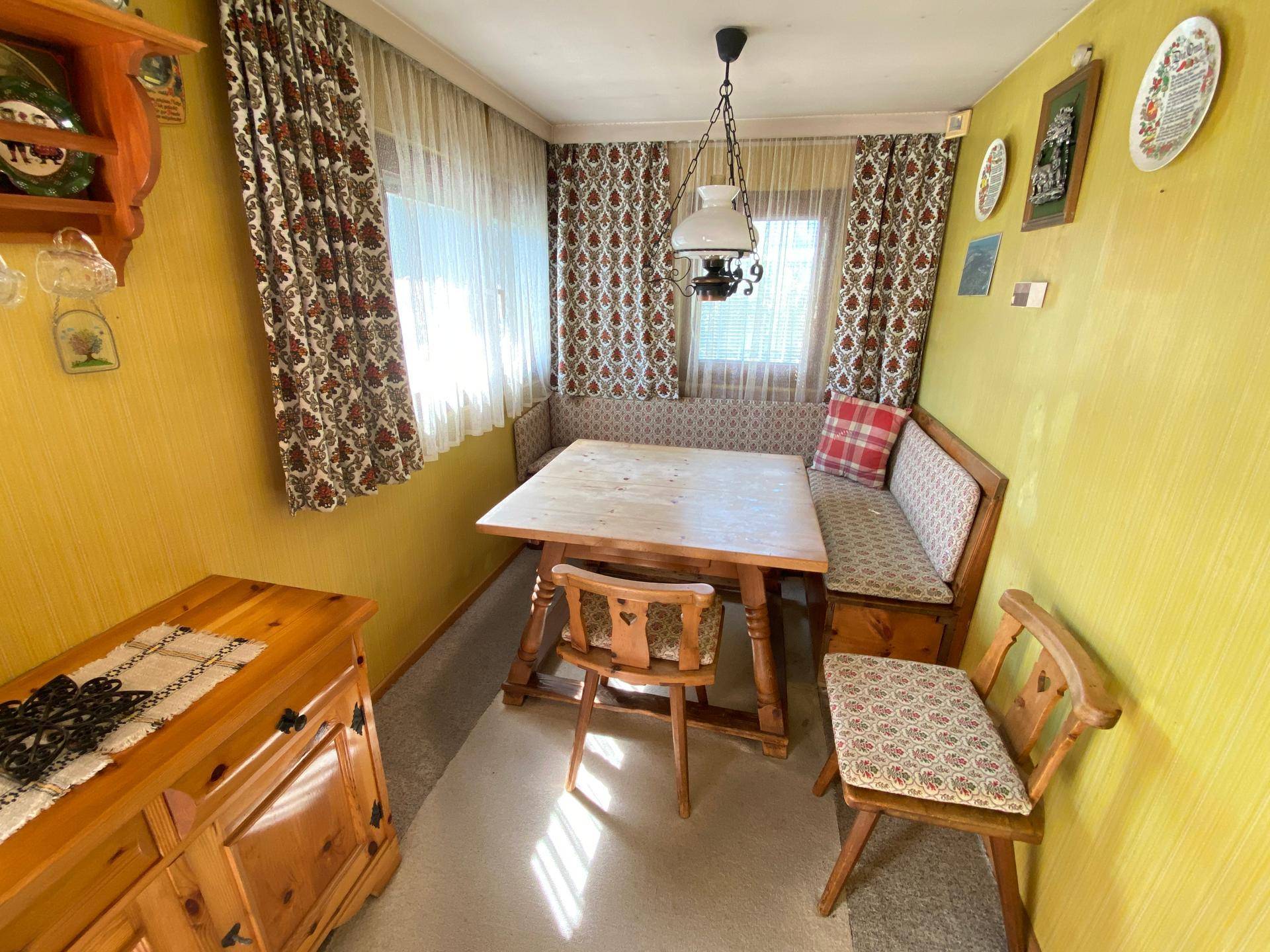 Gemütlicher Essbereich mit Holztisch, gepolsterter Eckbank und traditionellen Vorhängen, ideal für Mahlzeiten.