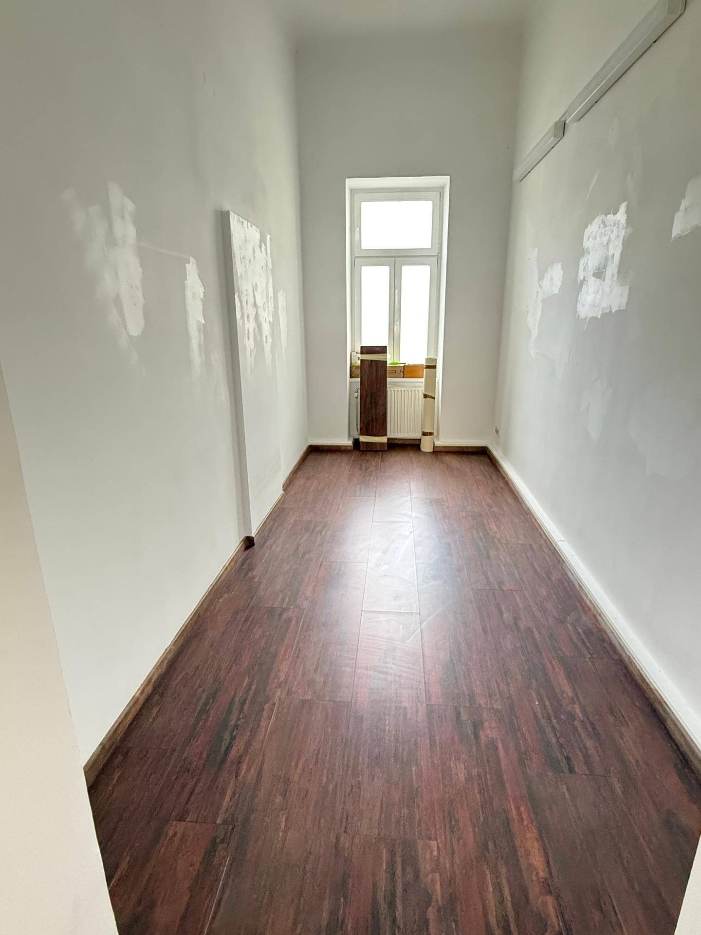 Langer, schmaler Raum mit dunklem Laminatboden und einem Fenster am Ende, ideal als Flur oder kleines Büro.