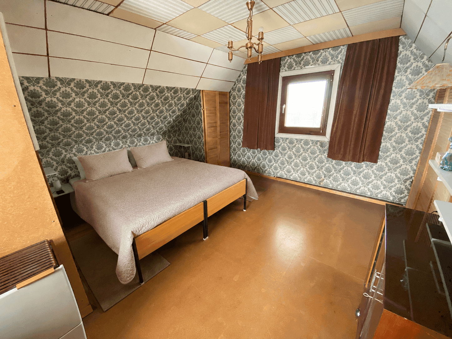 Gemütliches Schlafzimmer im Dachgeschoss mit schräger Decke, gemusterter Tapete und einem Doppelbett.