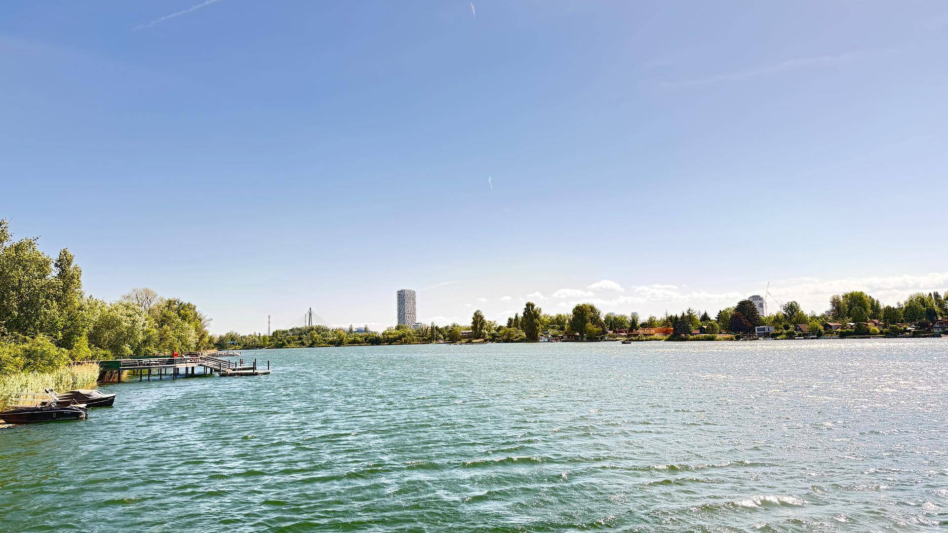 Weiter Blick über den See mit Anlegestellen und üppiger Vegetation am Ufer unter strahlend blauem Himmel.
