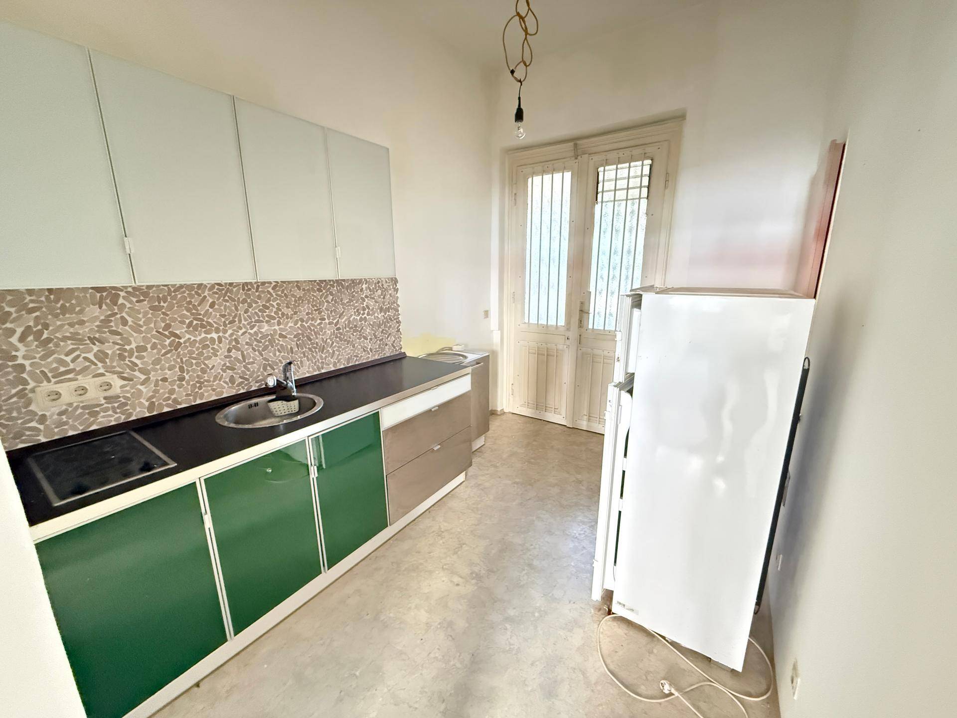 Küche mit grünen und weißen Schränken, Spüle und einem freistehenden Kühlschrank, mit Zugang nach draußen.