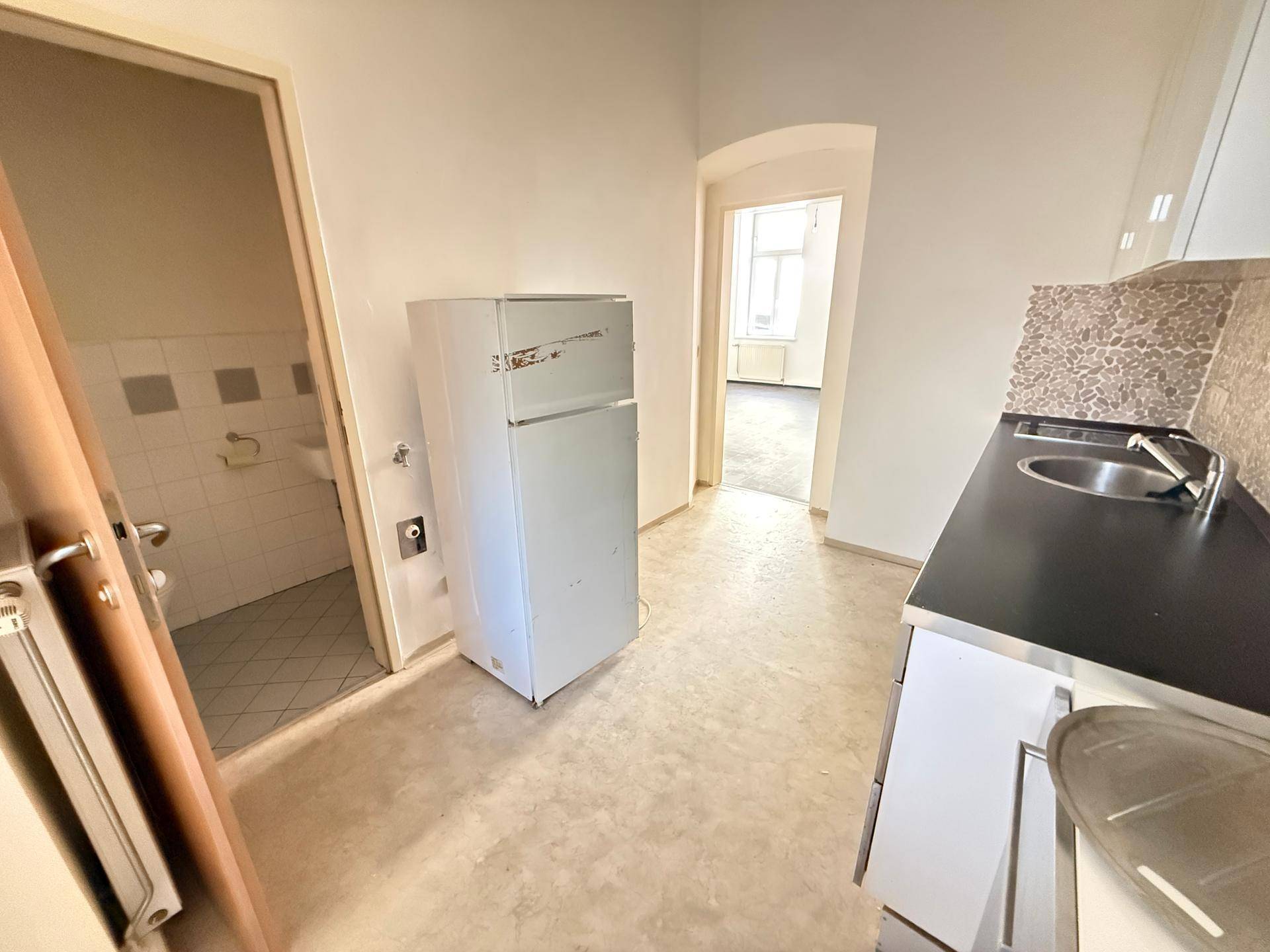 Küchenbereich mit Kühlschrank und Spüle, angrenzend an ein Badezimmer und einen weiteren Raum.