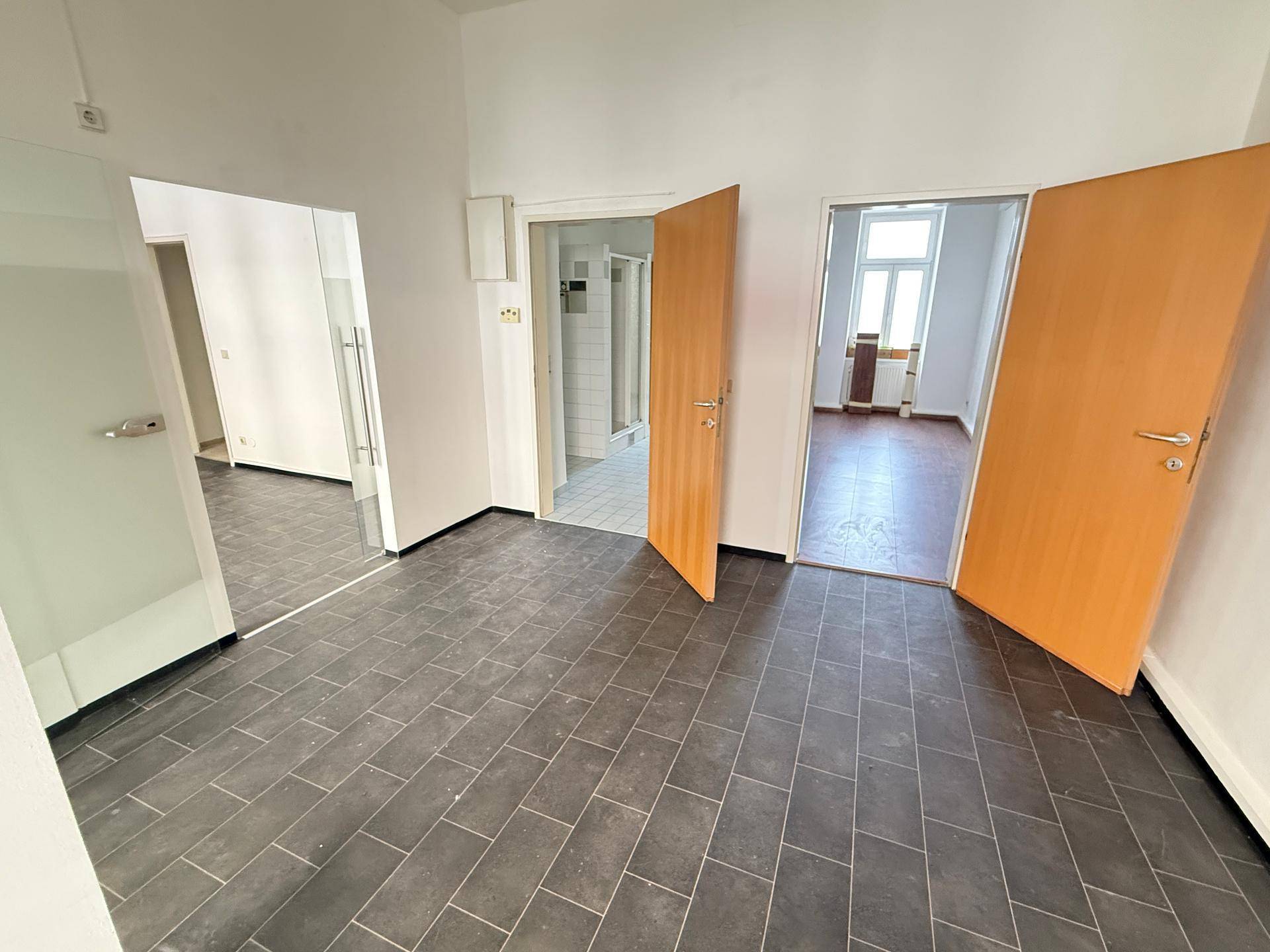 Geräumiger Bürobereich mit dunklen Fliesen, mehreren Türen und Blick in angrenzende Räume.