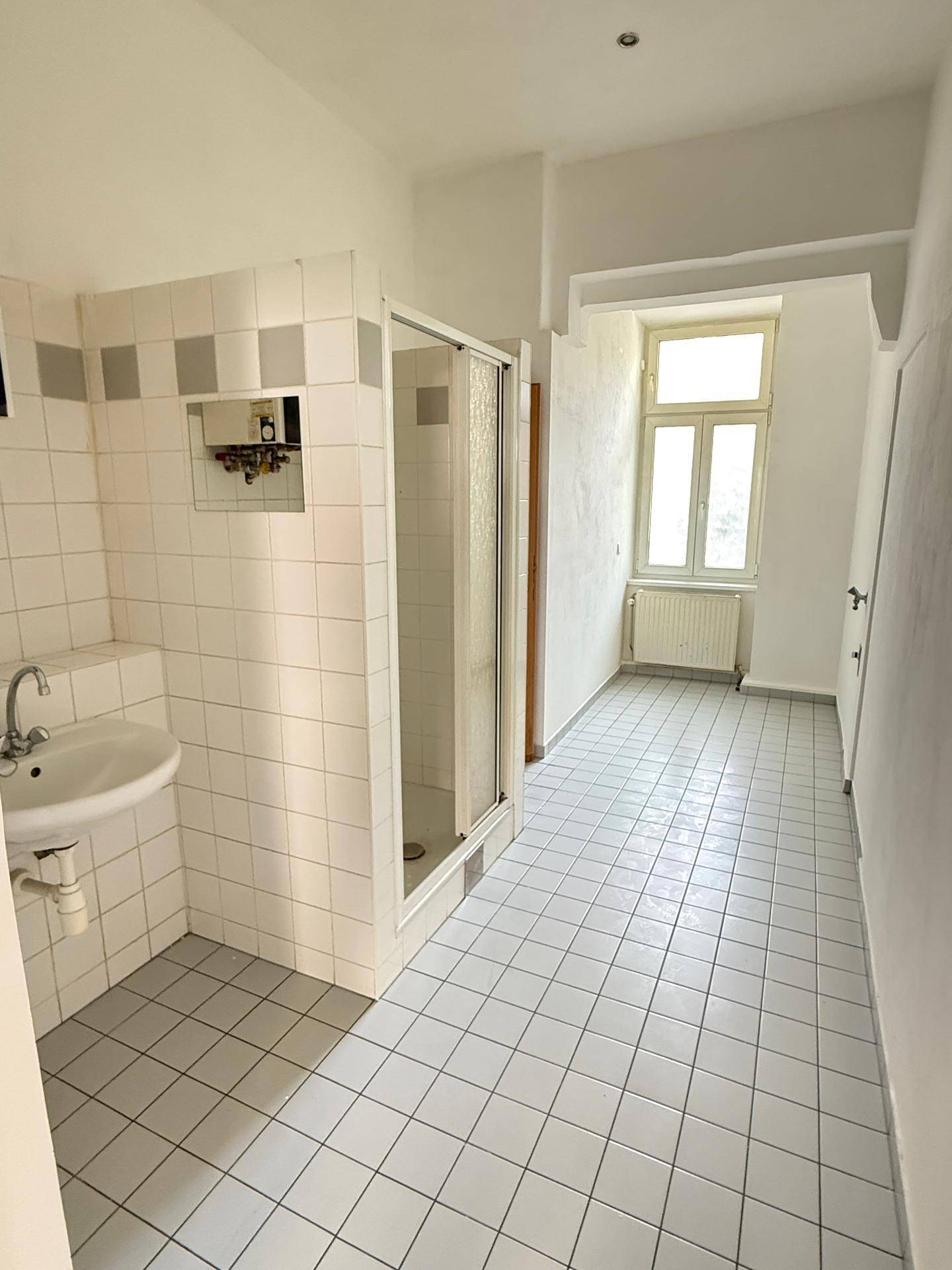 Badezimmer mit weißen Fliesen, Waschbecken und Duschkabine, hell durch ein großes Fenster.