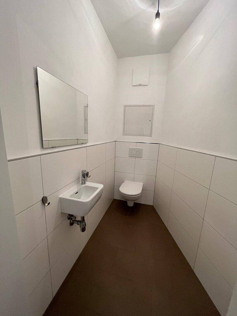 Modernes Gäste-WC mit weißen Fliesen, wandhängendem WC und kleinem Waschbecken.