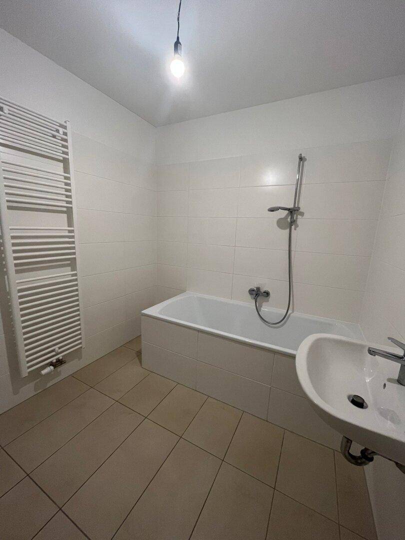 Modernes Badezimmer mit Badewanne, Waschbecken, beheiztem Handtuchhalter und hellen Fliesen.